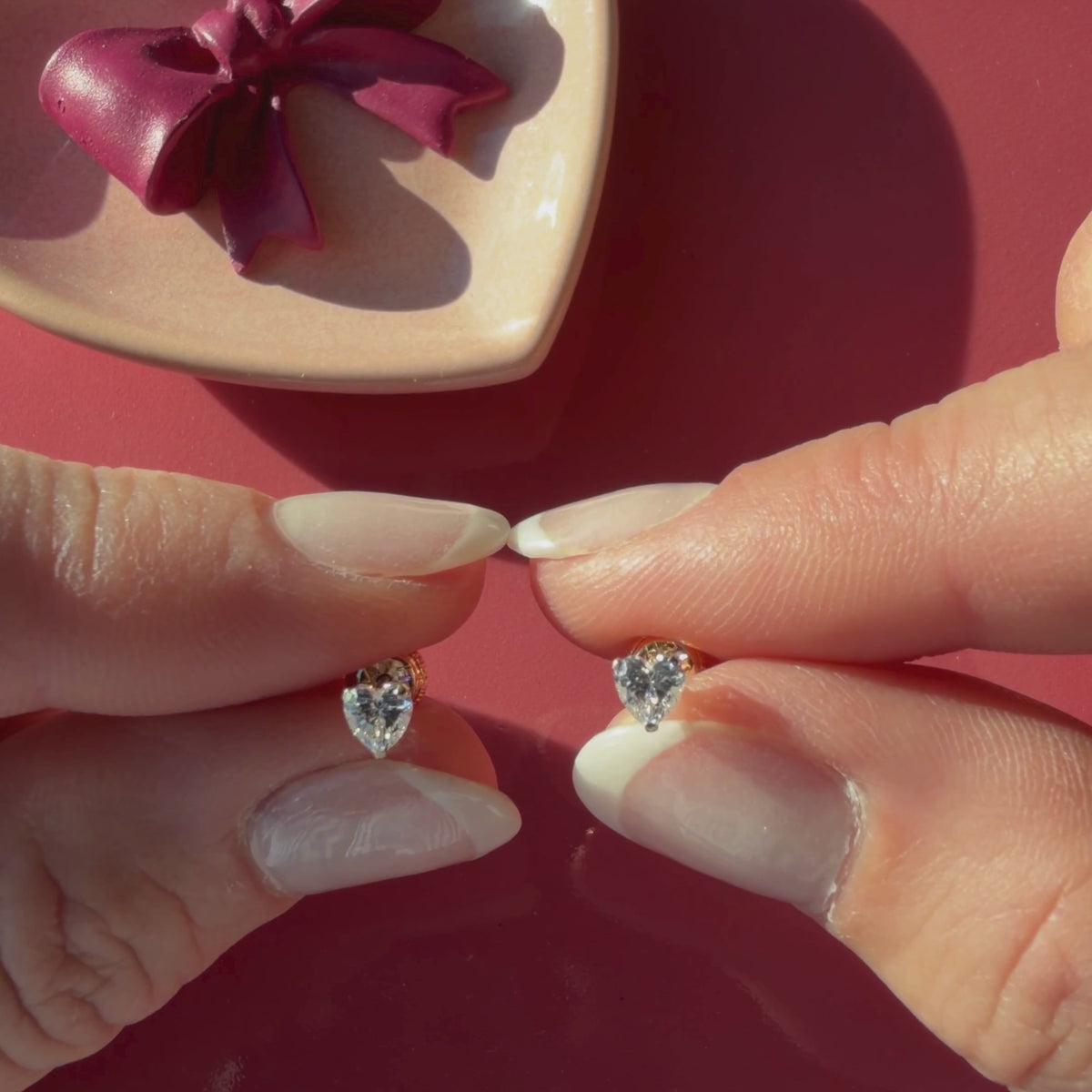 Video of Petite Heart clear heart CZ stud earrings in solid 14K yellow gold held in hand to show their actual size for babies and children.