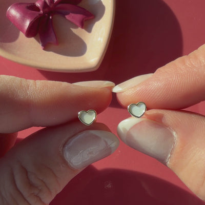 Video of Genuine Love mother of pearl heart stud earrings in solid 14K yellow gold held in hand to show their actual size for babies and children.
