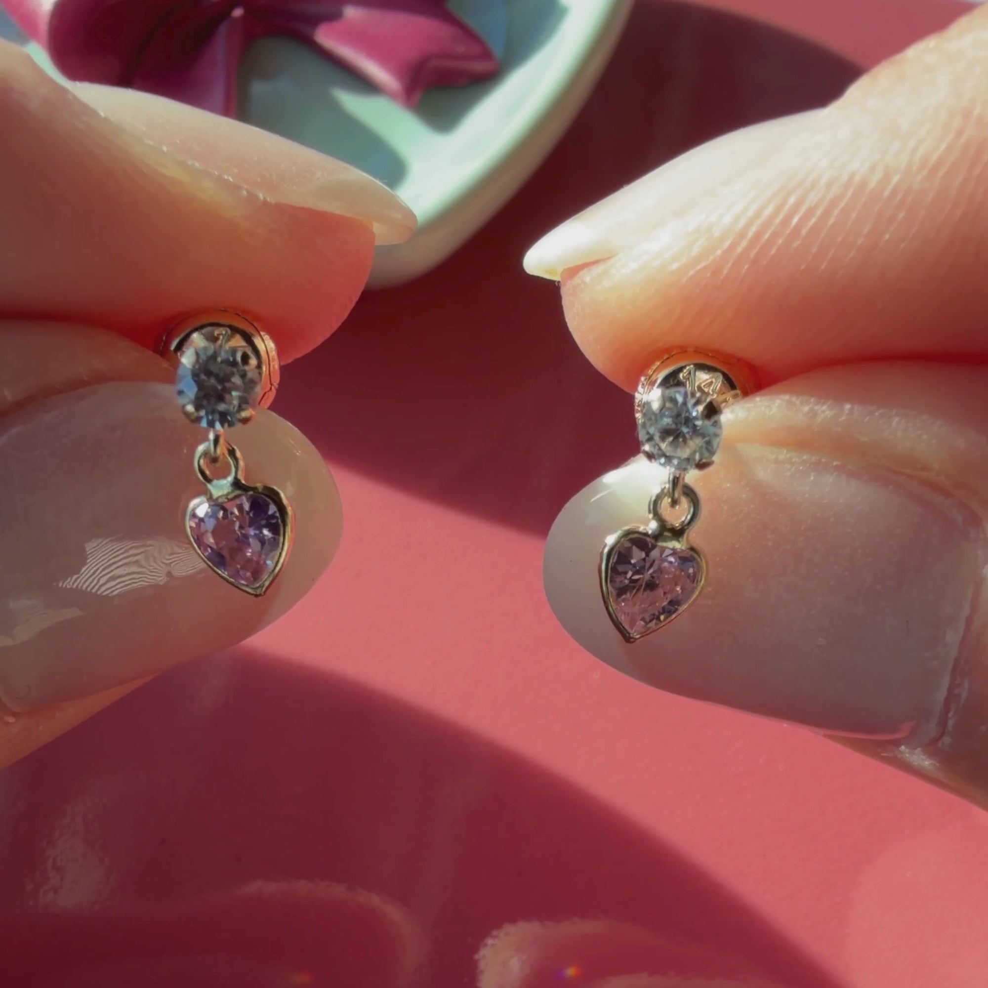 Video of Daring Heart pink and clear heart CZ dangle earrings in solid 14K yellow gold held in hand to show their actual size for babies and children.